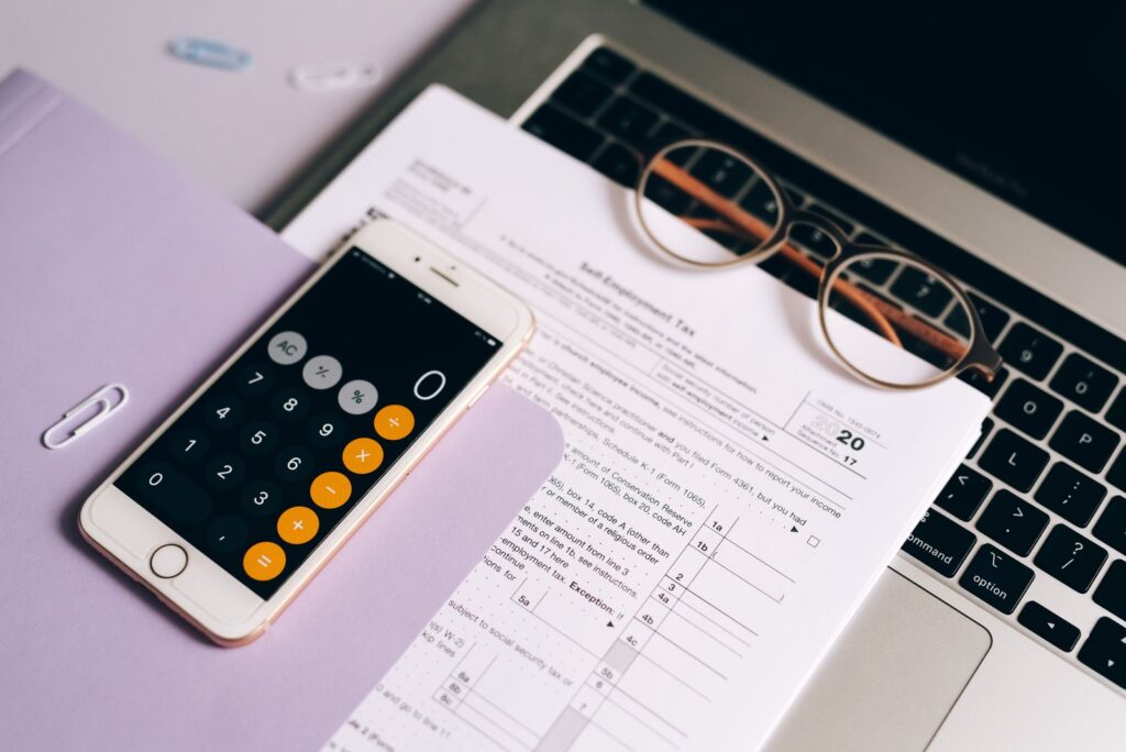 Calculadora en smartphone sobre documentos tributarios junto a un portátil